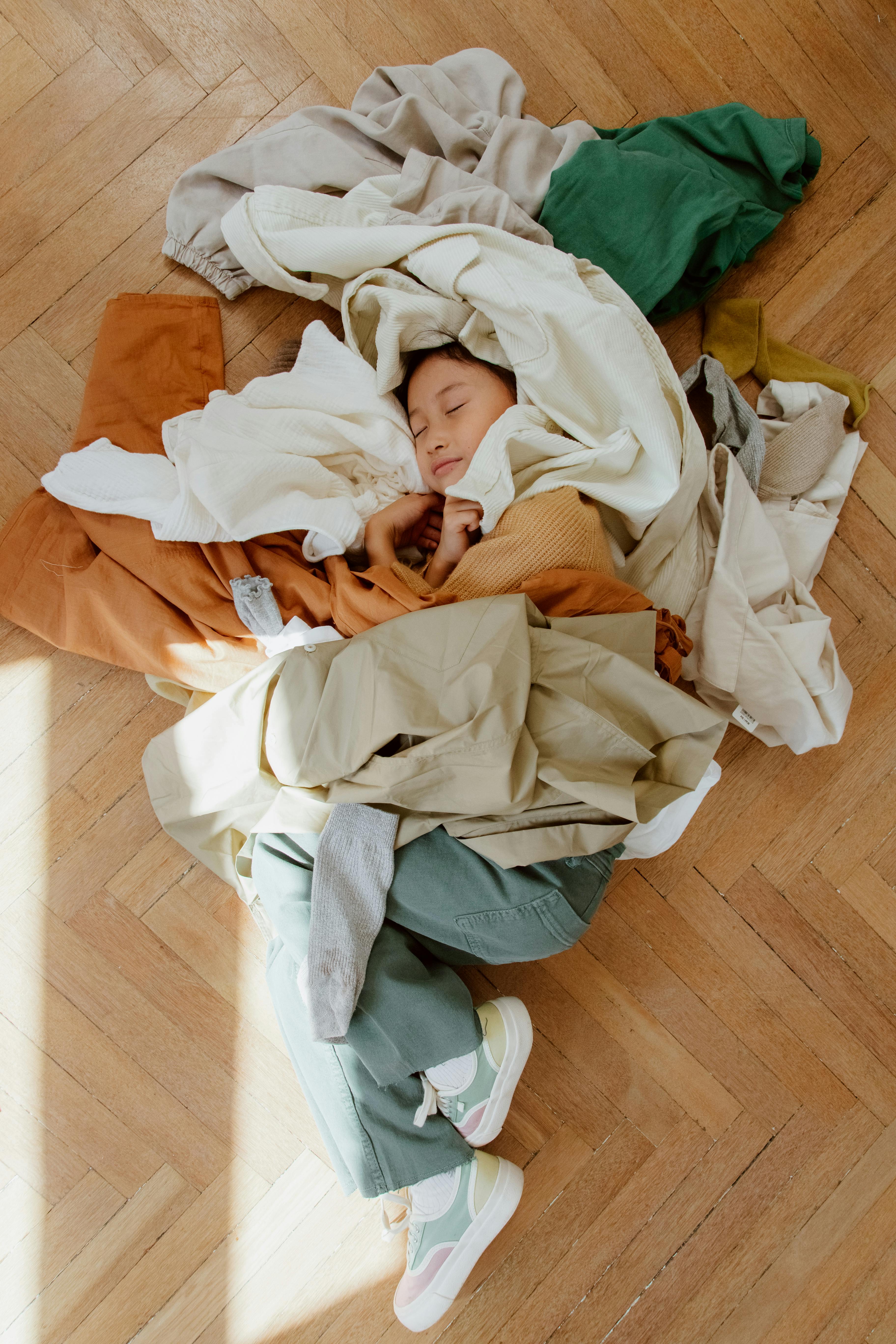 kid under pile of clothes on floor