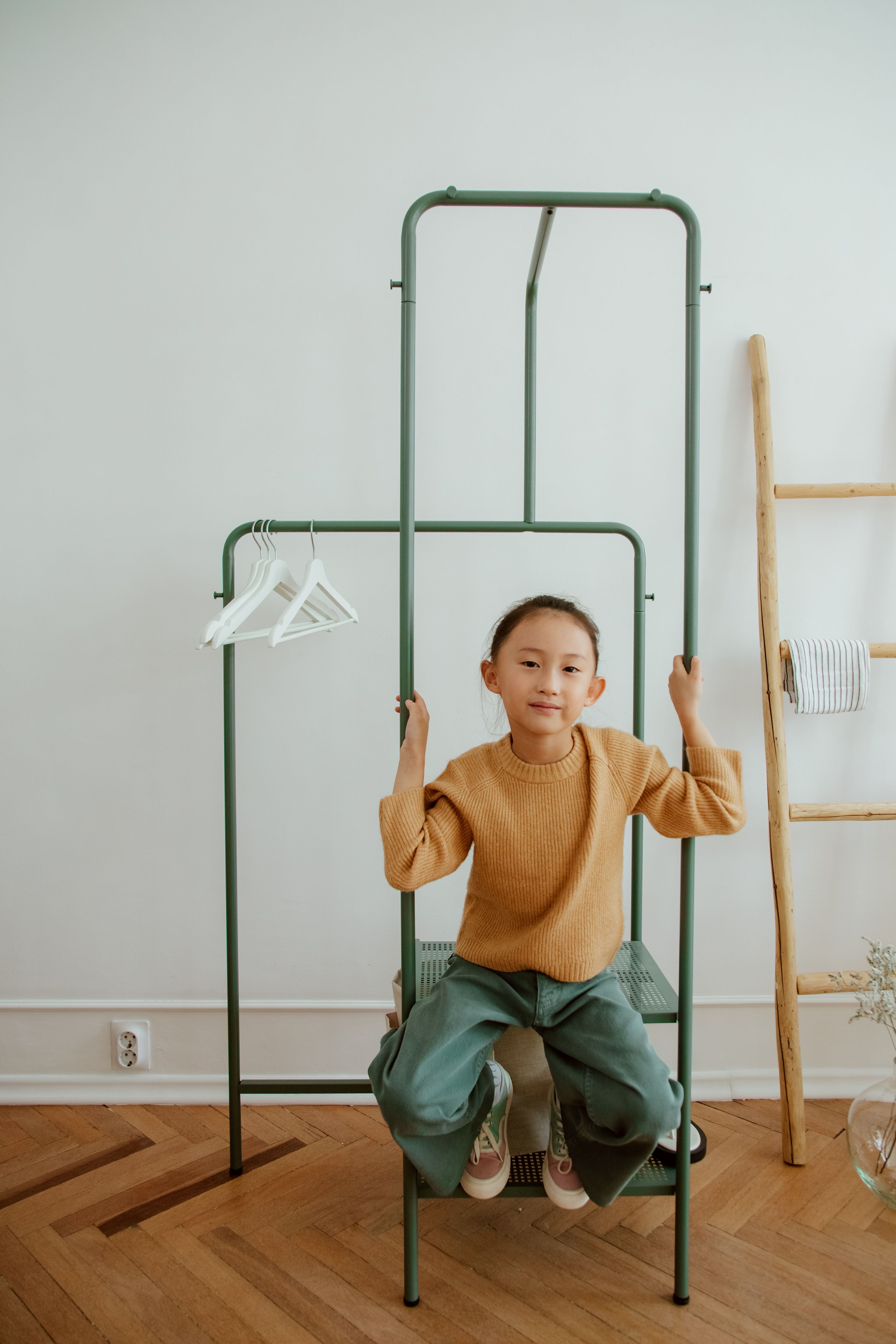 Young Girl Sitting on Clothing Rack · Free Stock Photo