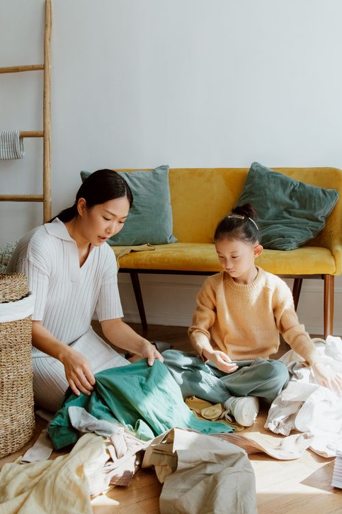 Free Asian mother and daughter sorting laundry together on the living room floor, showcasing family bonding and teamwork. Stock Photo