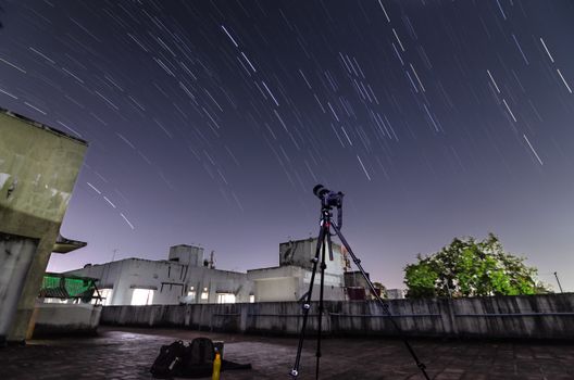 A telescope on a rooftop captures star trails in the night sky.