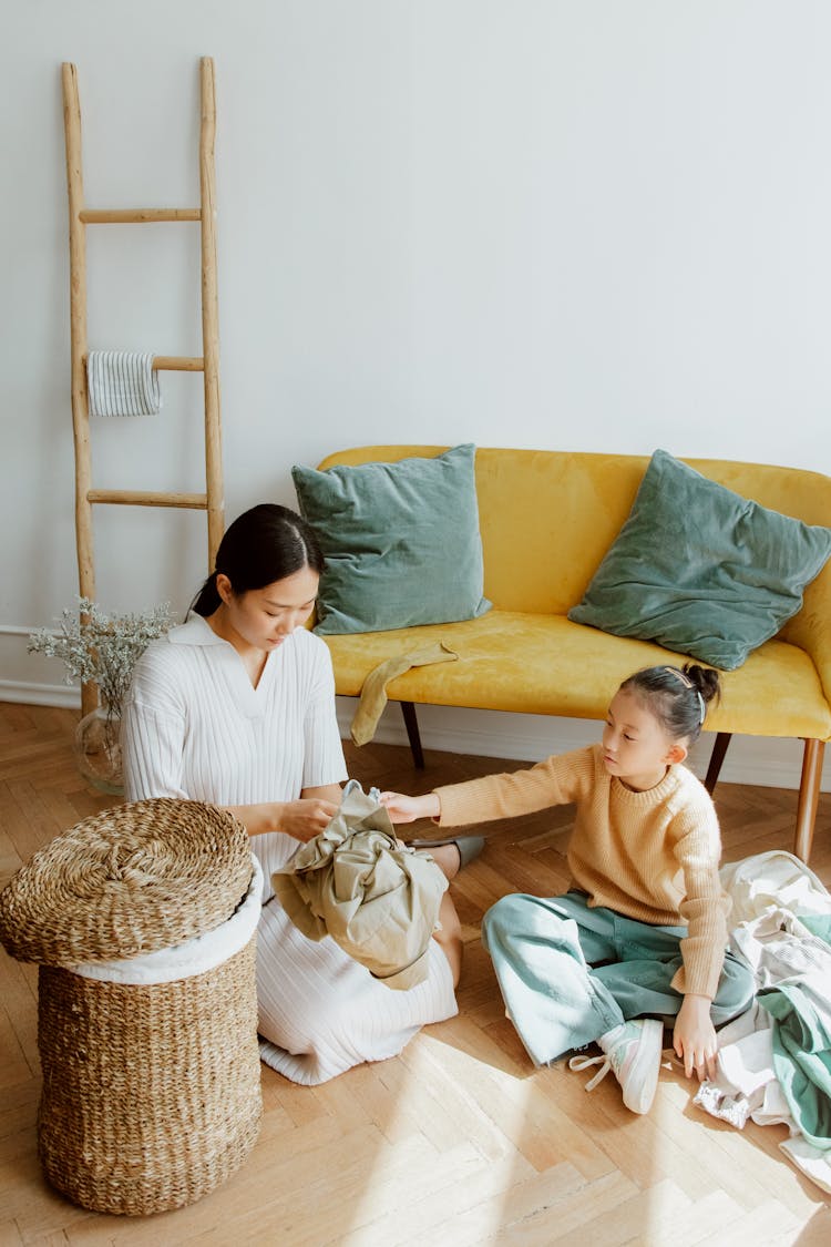 Mother And Daughter Cleaning Up Clothes Sitting On Floor