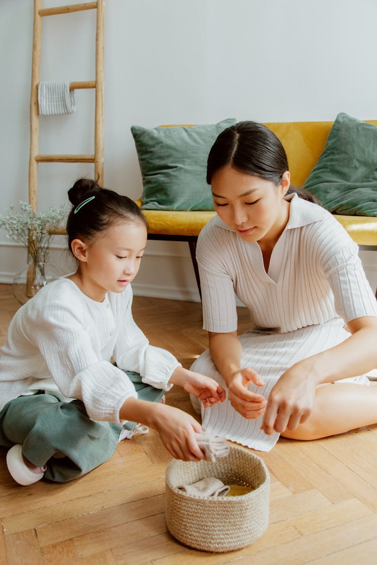 Mother And Daughter Cleaning Up Clothes In Living Room