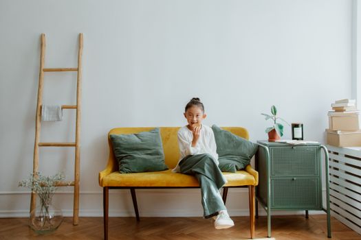 A child sitting on a yellow sofa in a stylish living room, enjoying a treat, surrounded by modern decor.