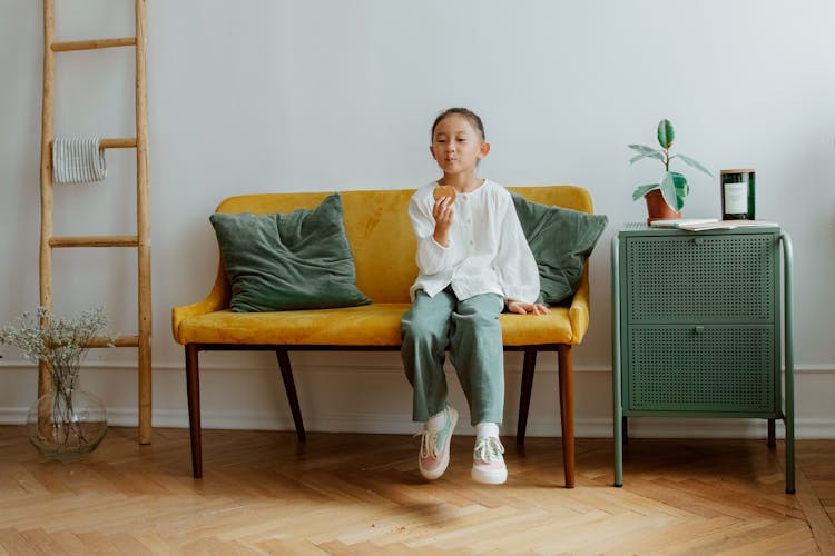 Girl Sitting On Sofa Eating Cookie