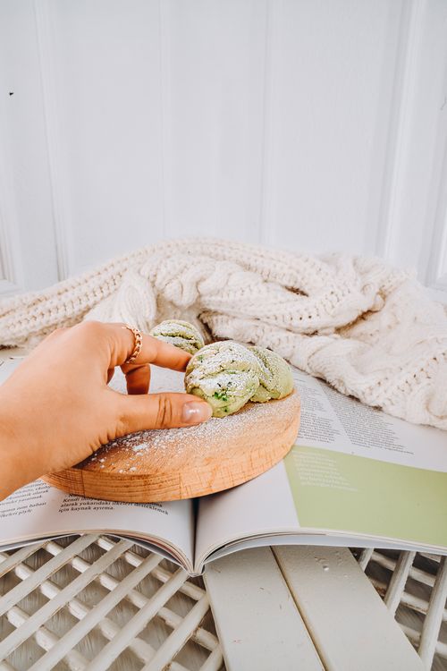 Free Aesthetic indoor shot of a hand reaching for matcha cookies on a wooden board, with a knitted blanket and magazine. Stock Photo