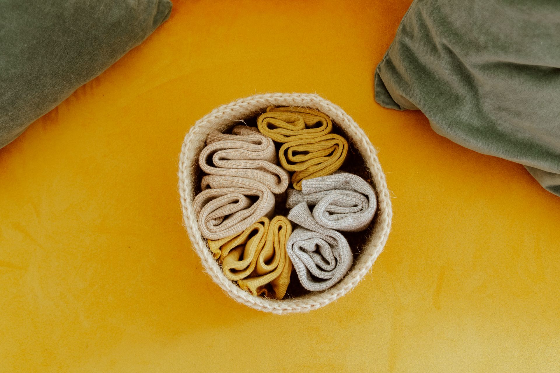 Top-down view of neatly arranged woolen socks in a basket on a vibrant yellow surface.