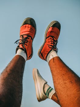 Creative low angle shot of legs in colorful sneakers against a clear sky, showcasing style and energy.