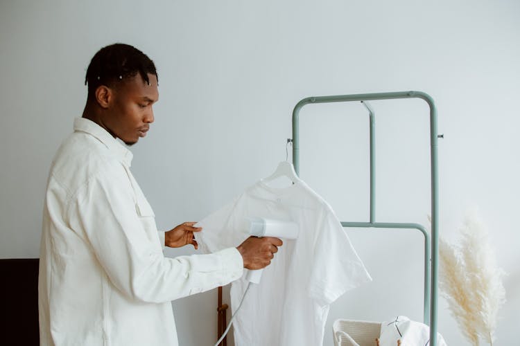 Man Steam Ironing Shirt Hanging From Clothing Rack