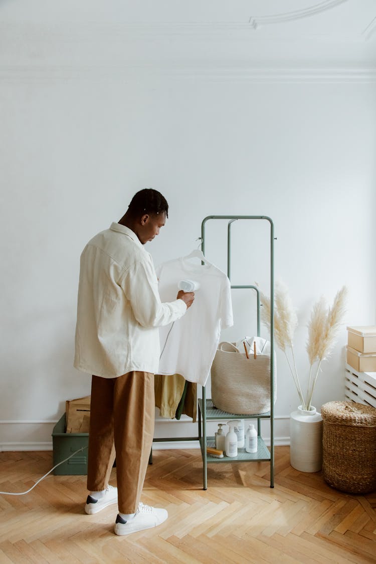 Man Steam Ironing Shirt Hanging From Clothing Rack