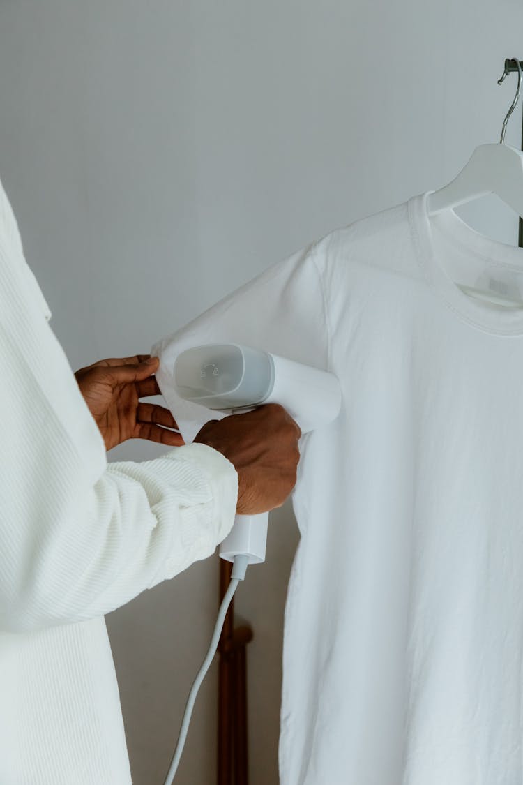 Man Steam Ironing Shirt Hanging From Clothing Rack