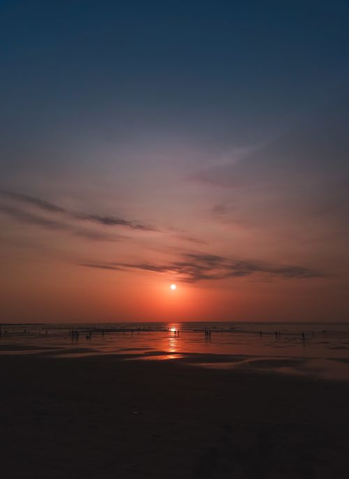 Free Breathtaking beach scene capturing a serene sunset and silhouettes over the ocean horizon. Stock Photo