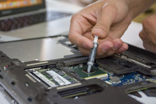 Hand of a Person Using s Syringe on a Computer Part