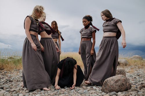 Woman in a Black Dress Kneeling on the Ground Surrounded by Group of Women in Gray Dresses