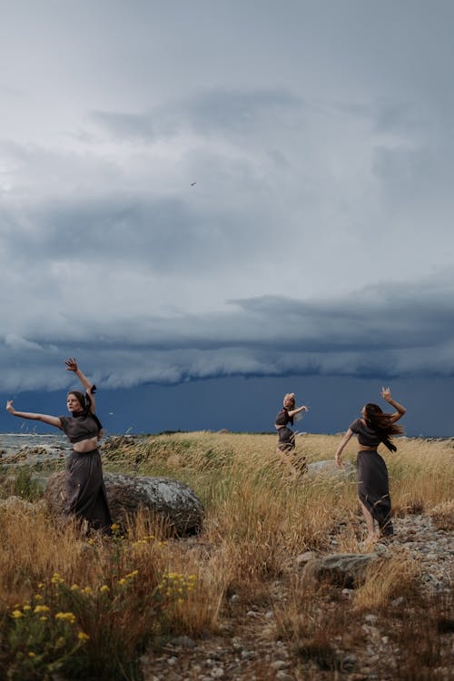 Women Posing on a Grass Field Under White Clouds