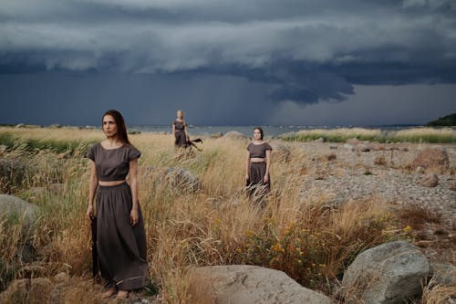 Women in Long Dress Standing on a Grass Field while Looking Afar