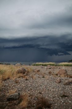 A stormy landscape with dark clouds looming over a pebble beach, creating a dramatic scene.