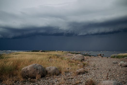 A dramatic coastal scene featuring storm clouds looming over a rocky seashore, with waves crashing against the rocks.