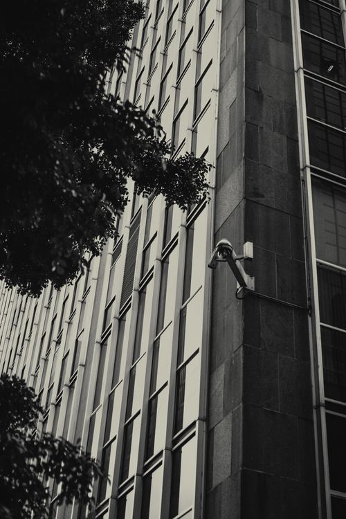 Free Black and white image of a modern building facade featuring a security camera. Stock Photo