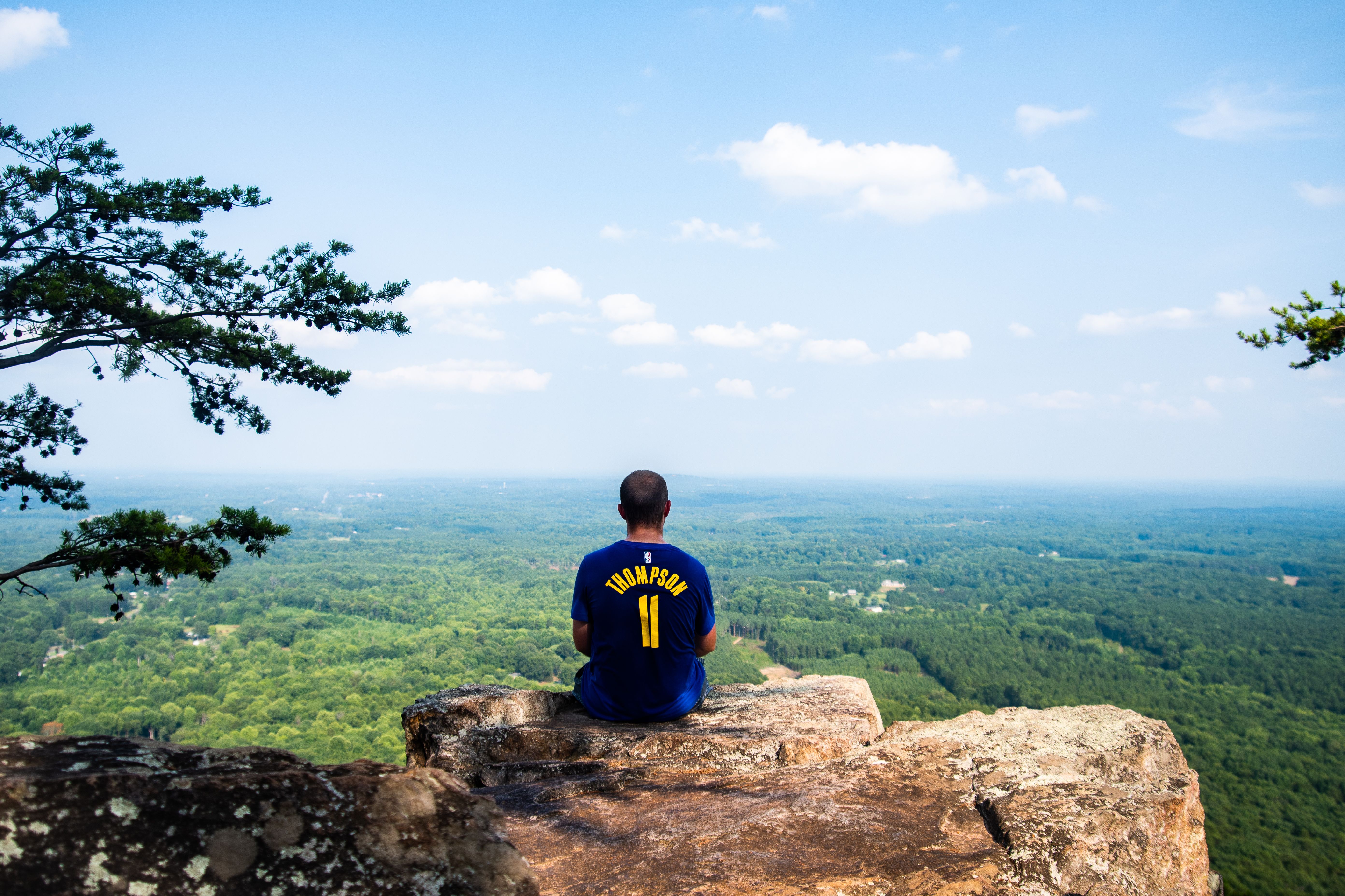 Man sitting on a rocky cliff enjoying a panoramic mountain view under a clear sky.