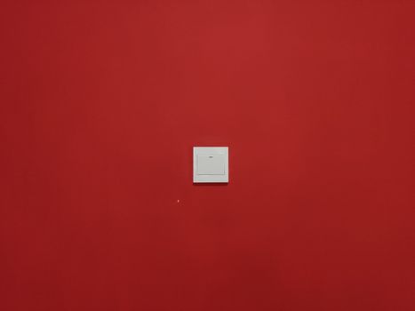A minimalist light switch centered on a bold red wall captures simplicity.
