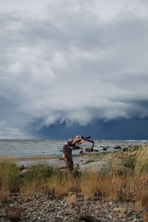 Woman Dancing on a Shore under Dark Clouds 