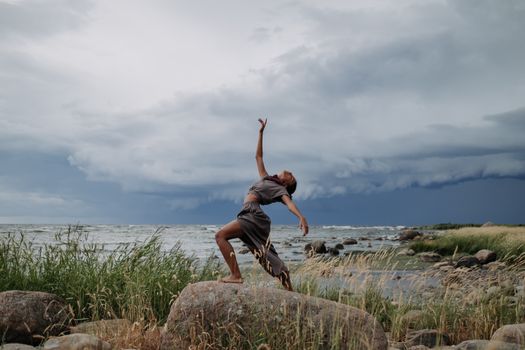 A woman performs a captivating dance on rocky seashore amidst dramatic storm clouds.