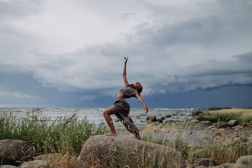 Free A woman performs a captivating dance on rocky seashore amidst dramatic storm clouds. Stock Photo