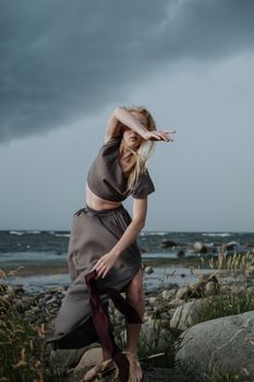 A woman performing a graceful contemporary dance by a stormy seashore.