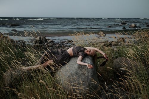 Free Woman in relaxed pose on rocky coastal landscape, evoking tranquility and connection with nature. Stock Photo