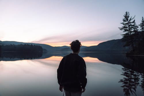 Back View of a Man in Black Jacket Standing in Front of the Lake during Sunset