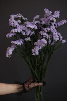 A hand in lace gloves holds a bouquet of vibrant purple sea lavender against a black background.