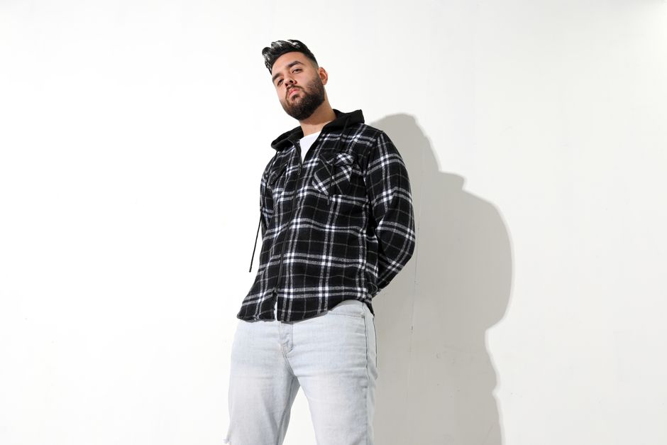 A stylish man in a plaid shirt poses confidently against a plain background, exuding a cool and casual vibe.