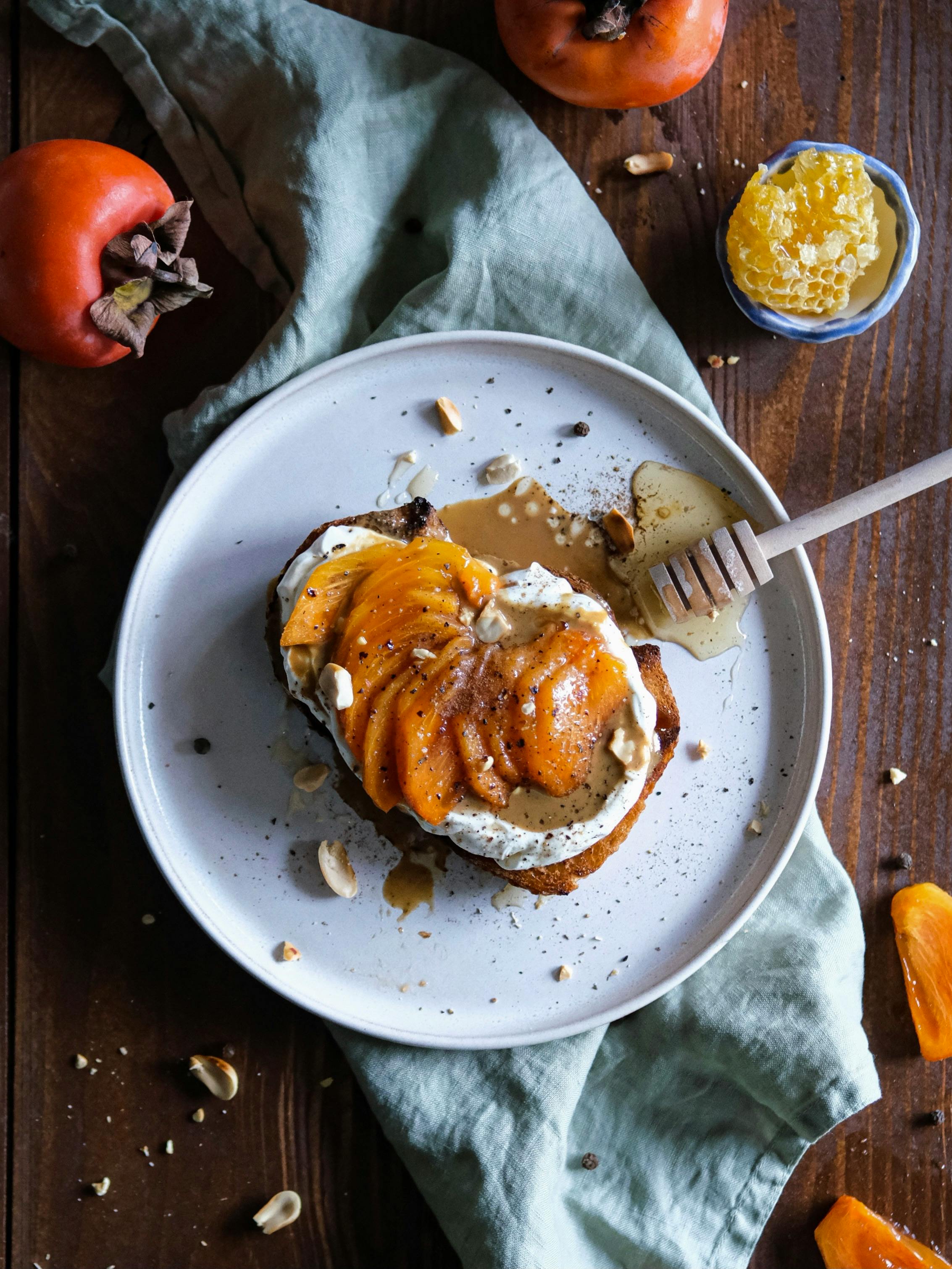 Tasty sliced persimmons on toast garnished with honey and nuts, perfect for a sweet treat.