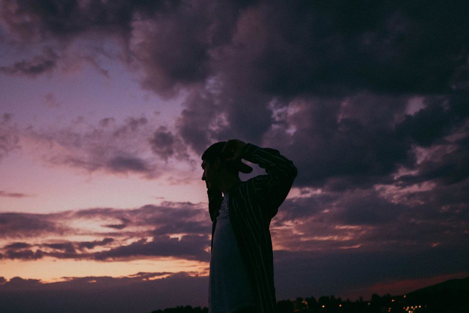A silhouette of a man wearing a cap against a dramatic purple evening sky.