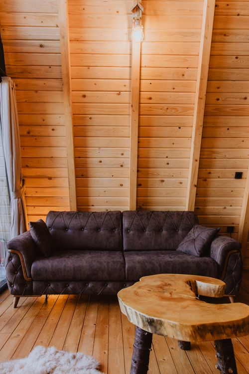 Free Warm wooden interior featuring a cozy sofa and uniquely shaped wooden table, perfect for relaxation. Stock Photo
