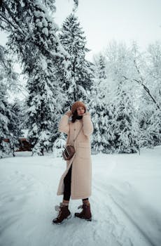 Woman in winter coat enjoying snowy scenery among snow-covered trees.