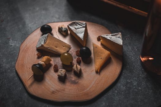 A rustic cheese platter with assorted cheeses, nuts, and grapes on a wooden board.