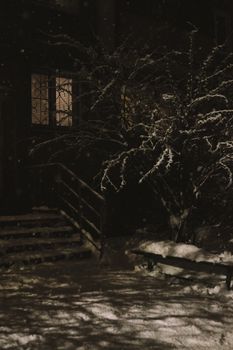 A peaceful snowy night scene with a lit window and dark shadows.