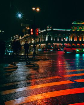 Illuminated street scene in Saint Petersburg showing vibrant nightlife with reflections on wet roads.