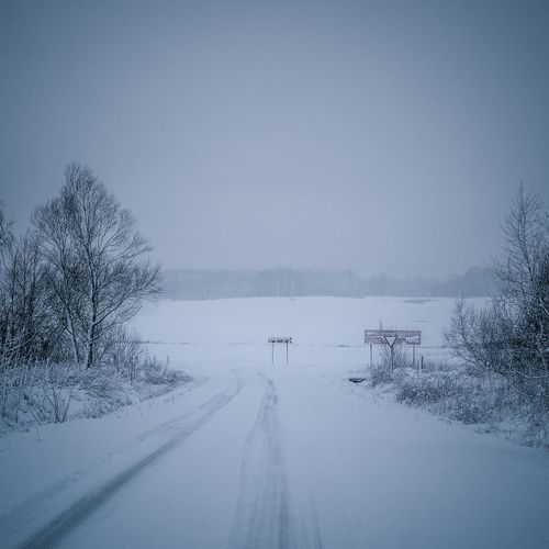 Free Tranquil winter landscape with snow-covered road and trees creating a serene atmosphere. Stock Photo