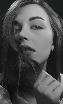 Close-up black and white portrait of a woman with a contemplative expression and hair framing her face.
