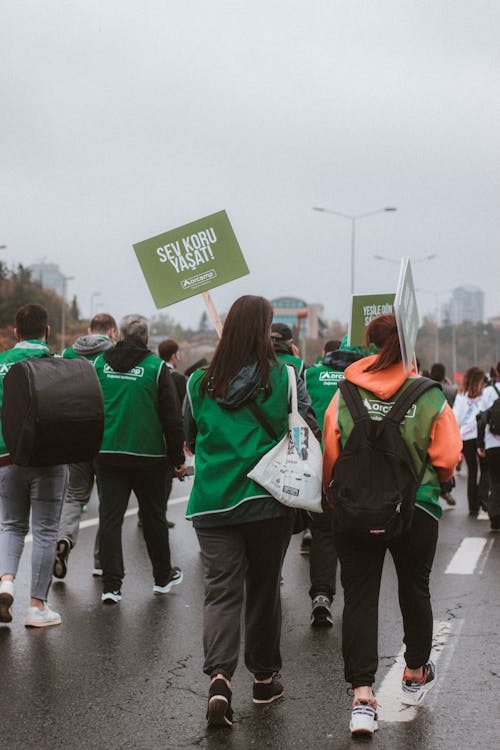 People in Green Vest Holding Banner while Walking on the Wet Road