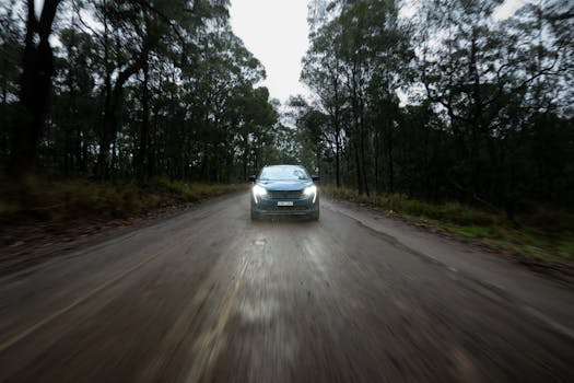 A car travels on a wet, secluded forest dirt road in NSW, Australia during dusk.