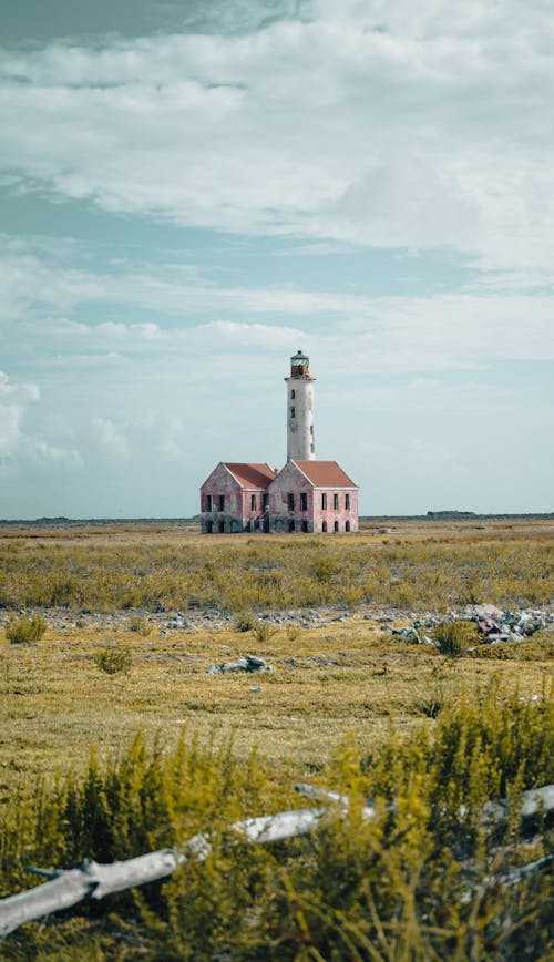 A Lighthouse and Concrete House on the Middle of a Grass Field