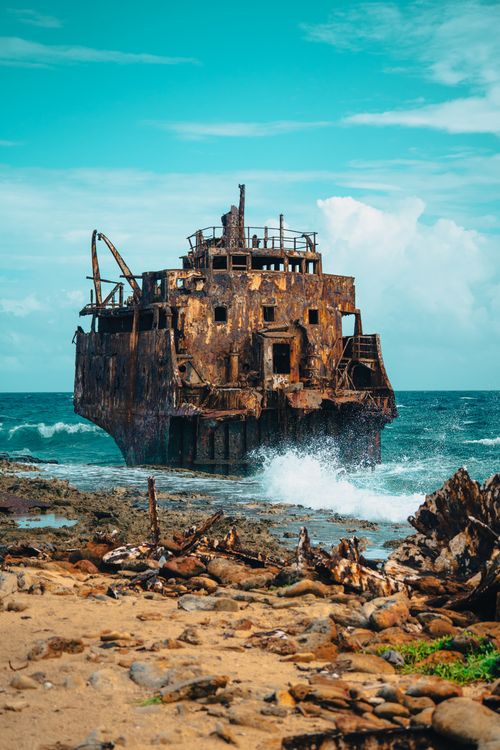Free A rusty shipwreck stands against the blue sea on a rocky shore, showcasing nature's beauty. Stock Photo