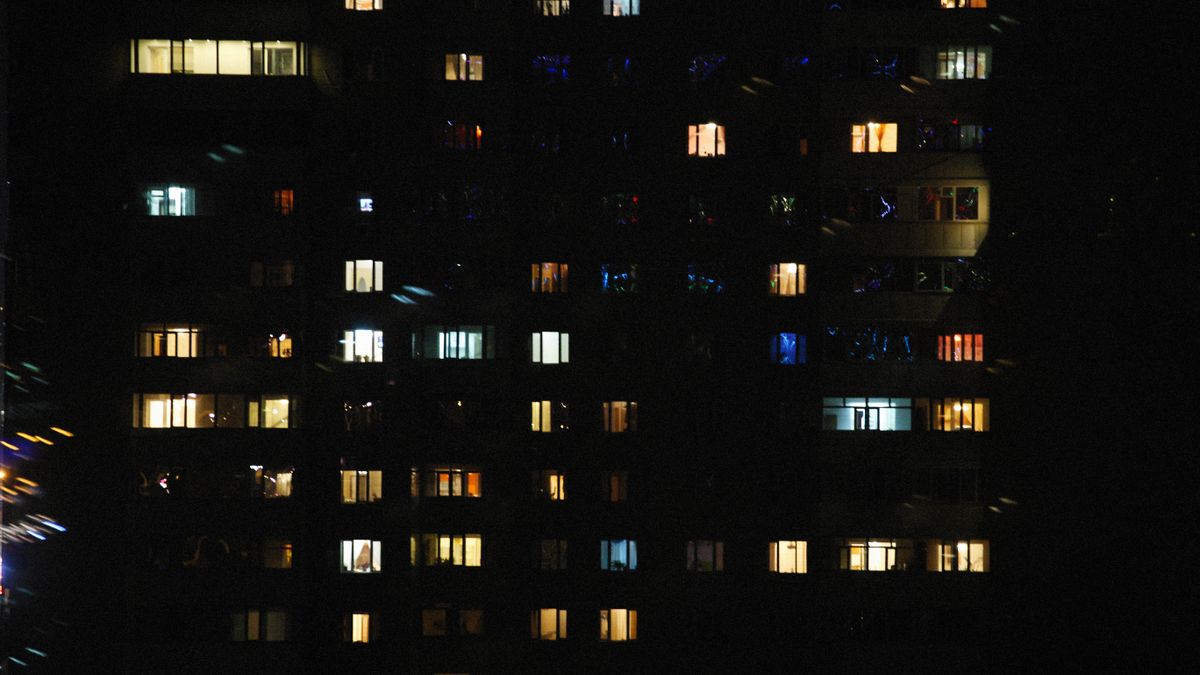 夜の集合住宅で多くの窓に灯りがついているイメージ