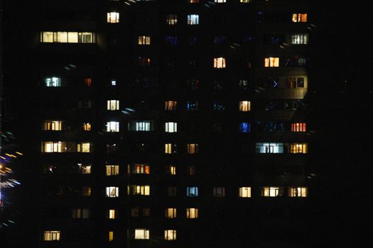 A night view of an urban high-rise with various illuminated windows, showcasing city life and architecture.