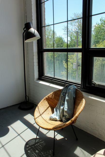 A loft with sunlight streaming through windows, showcasing a lamp, wicker chair, and denim jacket.