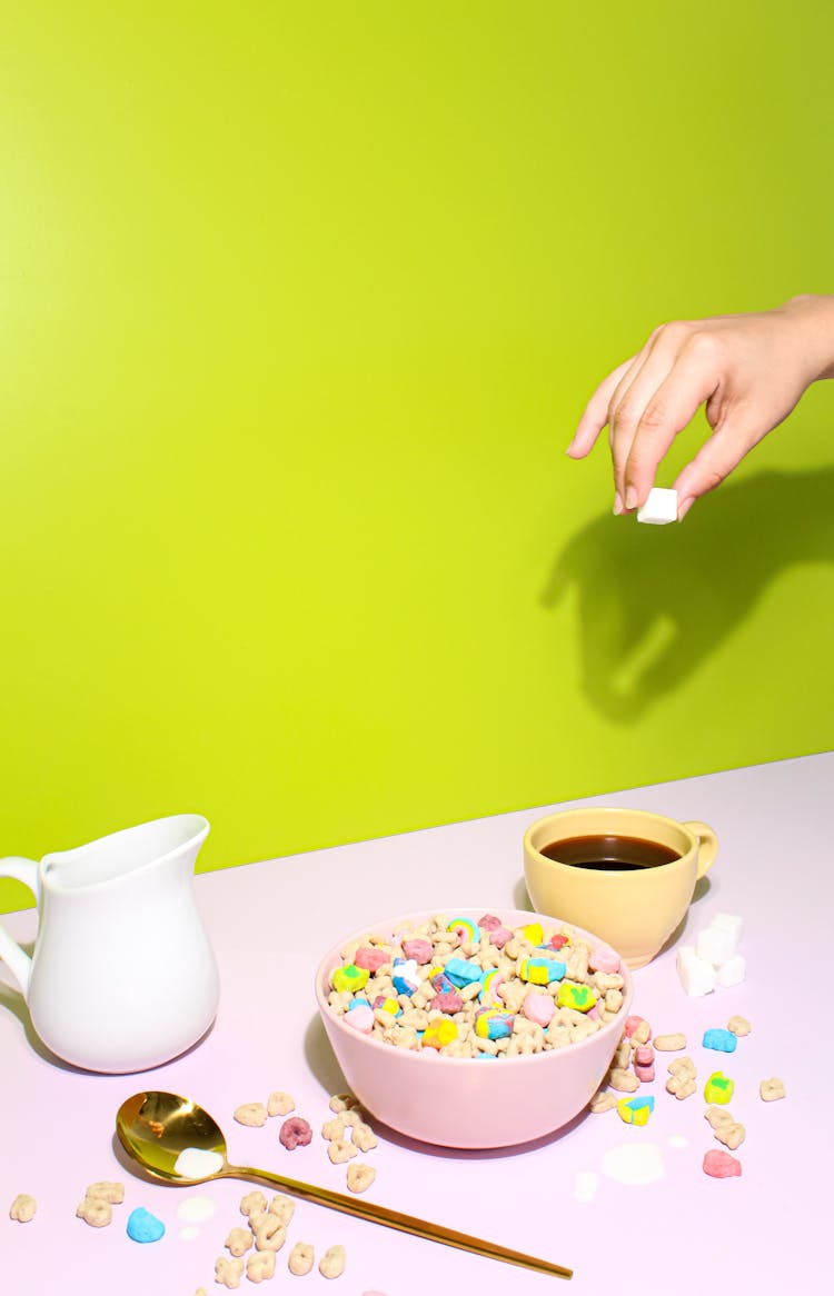 Hand Dropping Marshmallow Into Coffee Standing Next To Cereal Bowl