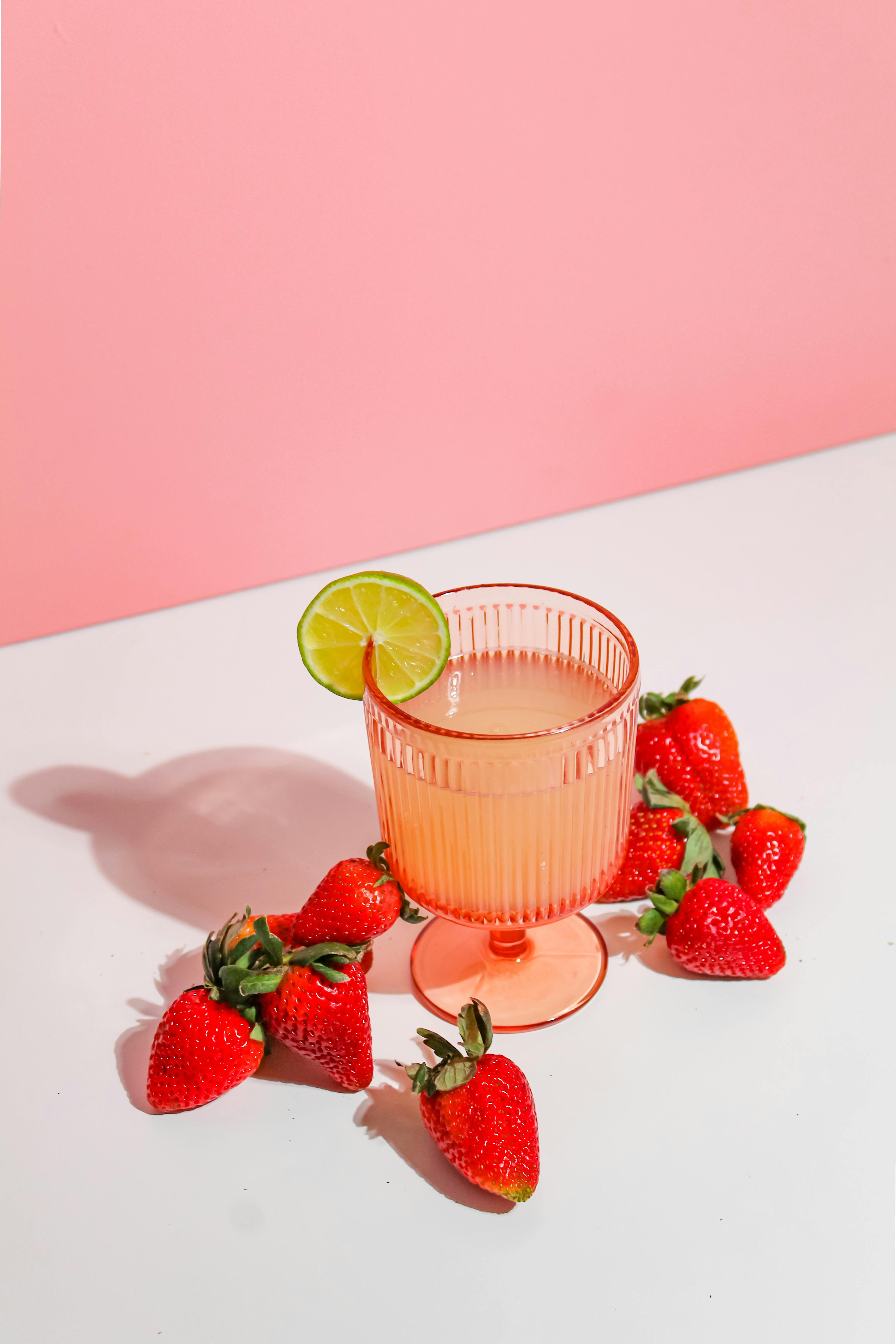 Chilled strawberry lime drink in a pink glass surrounded by fresh strawberries, perfect for summer refreshment.
